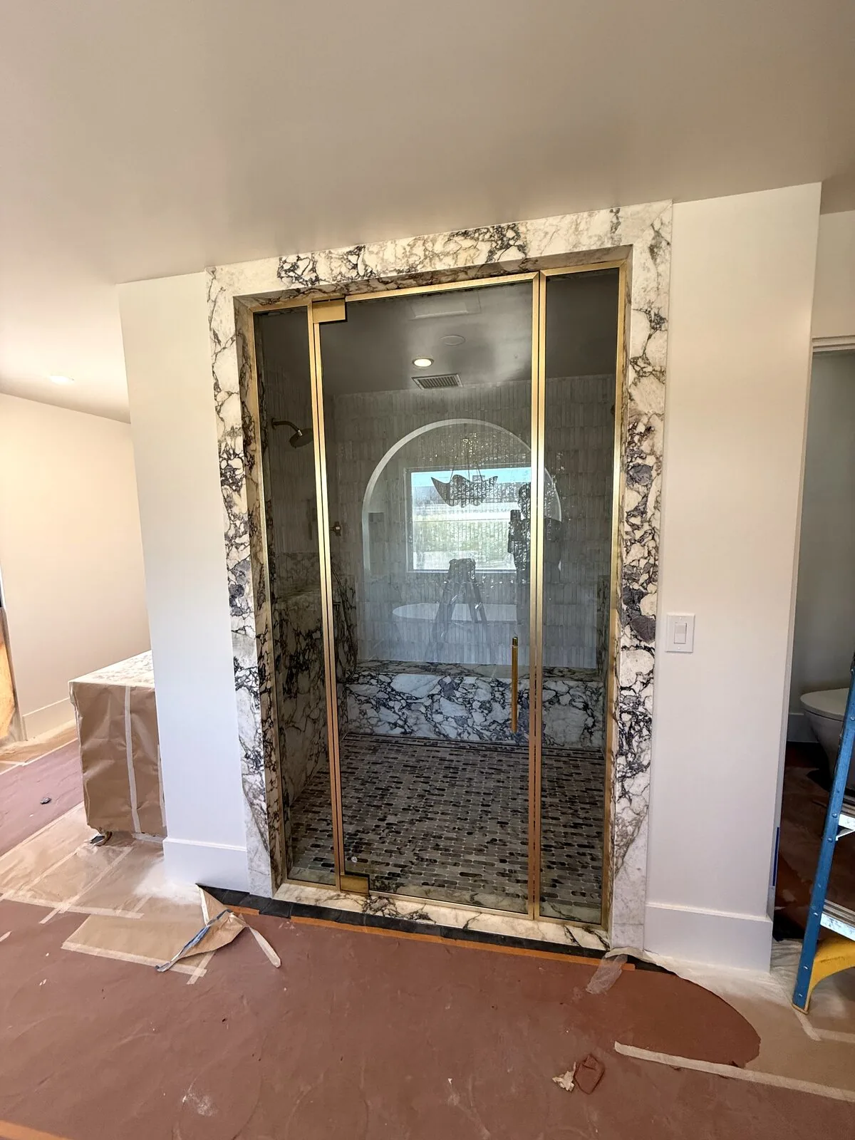 Marble steam shower with brass-framed glass door and arched interior, photographed during construction