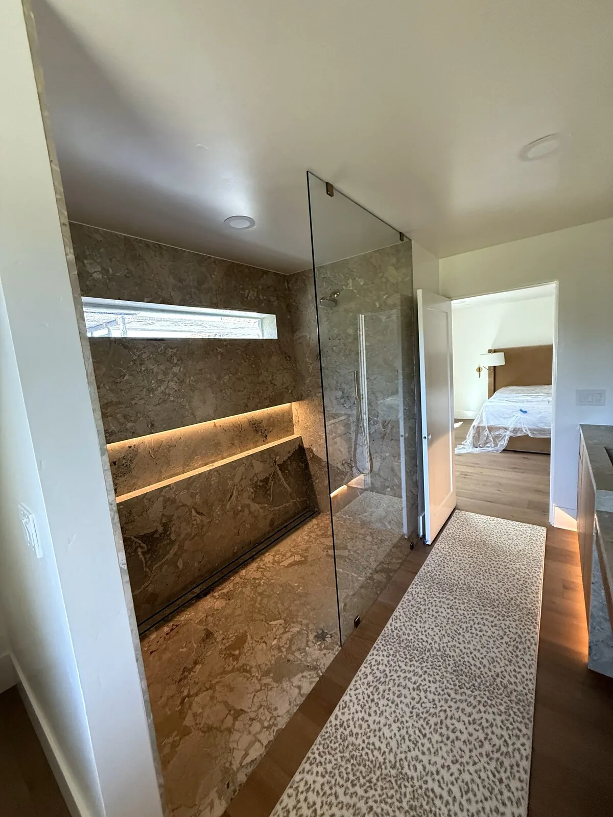 Walk-in shower with a frameless glass panel, stone walls, and a lighted niche in a Clovis luxury home