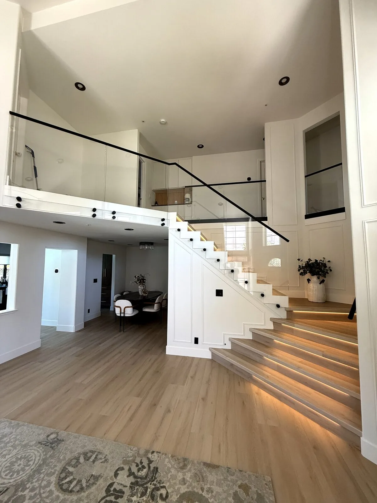 Staircase with tread lighting and frameless glass railing under a black handrail in a Folsom home