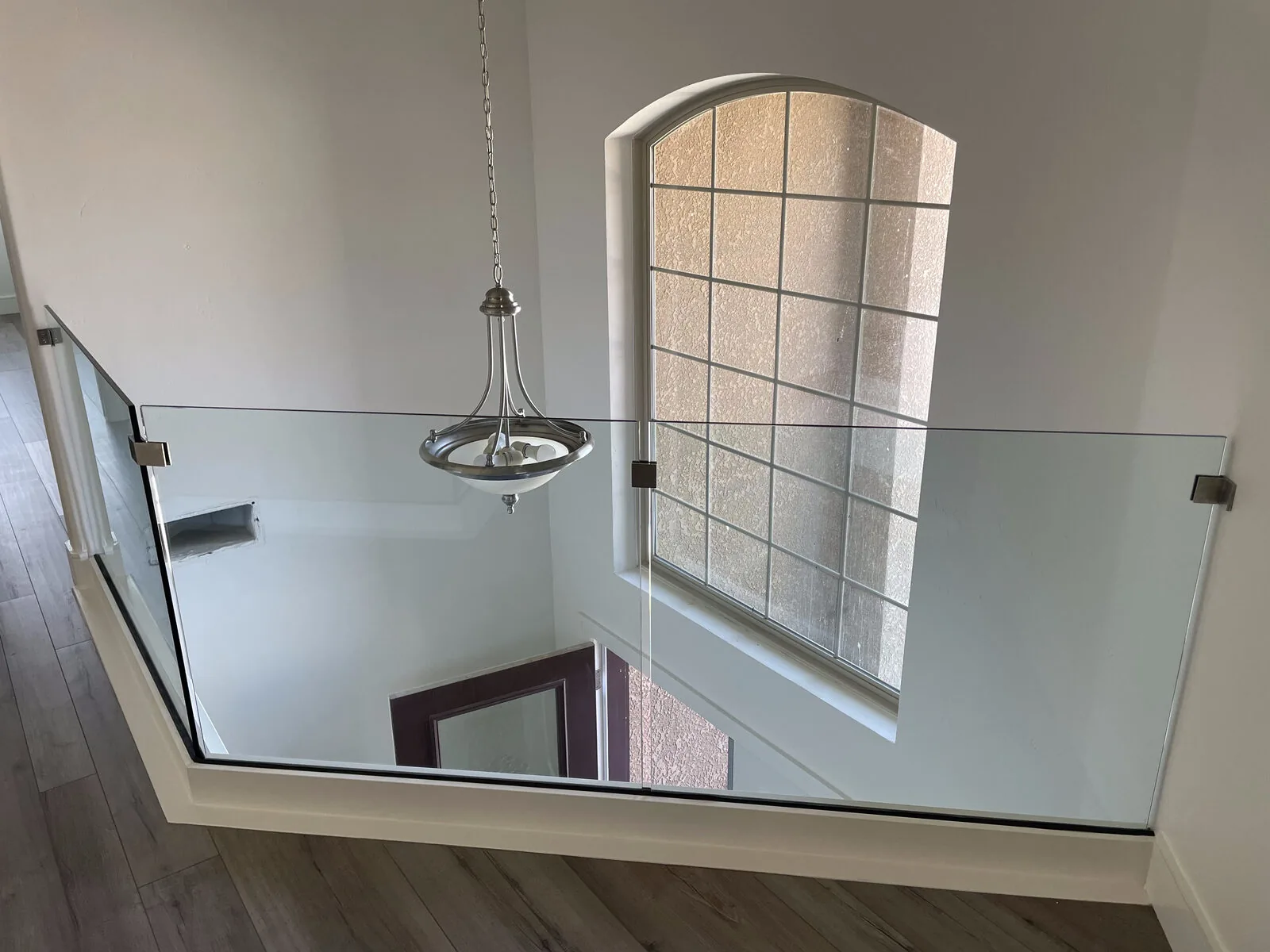 Wide view of the frameless glass landing railing with an arched window and pendant light