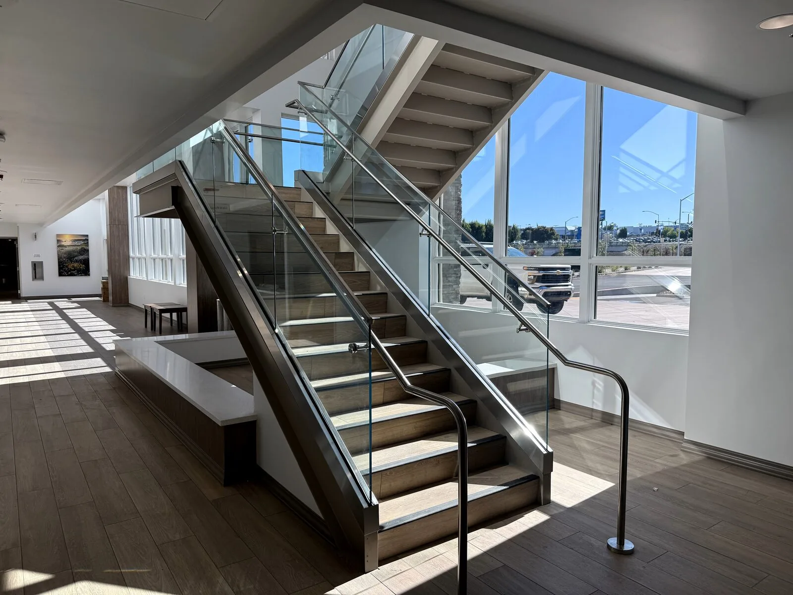 Main staircase of a health care building with glass railings and stainless handrails, daylight coming through full-height windows