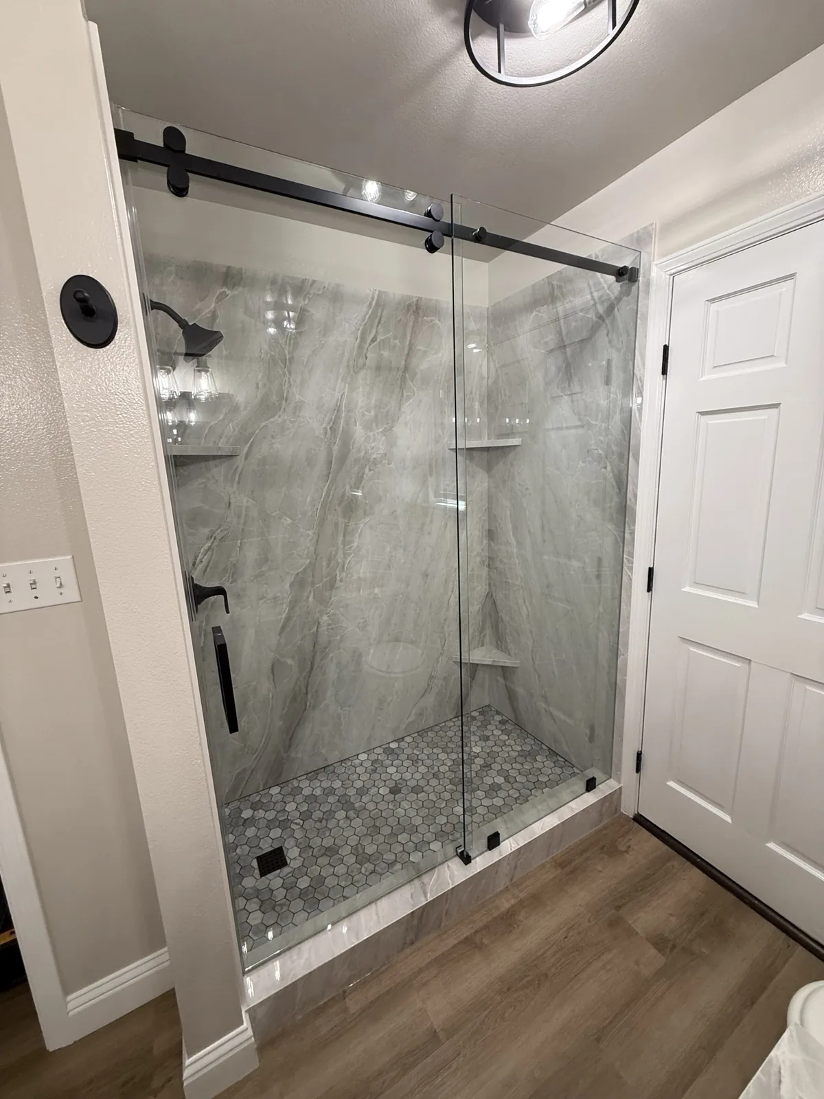 Frameless sliding glass shower door with matte black barn-style hardware over marble-look tile