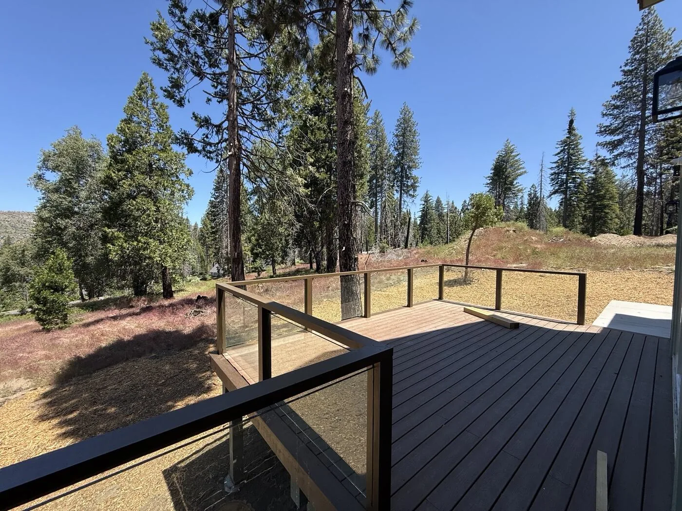 Wood-post railing with glass infill panels on a composite deck surrounded by pine forest