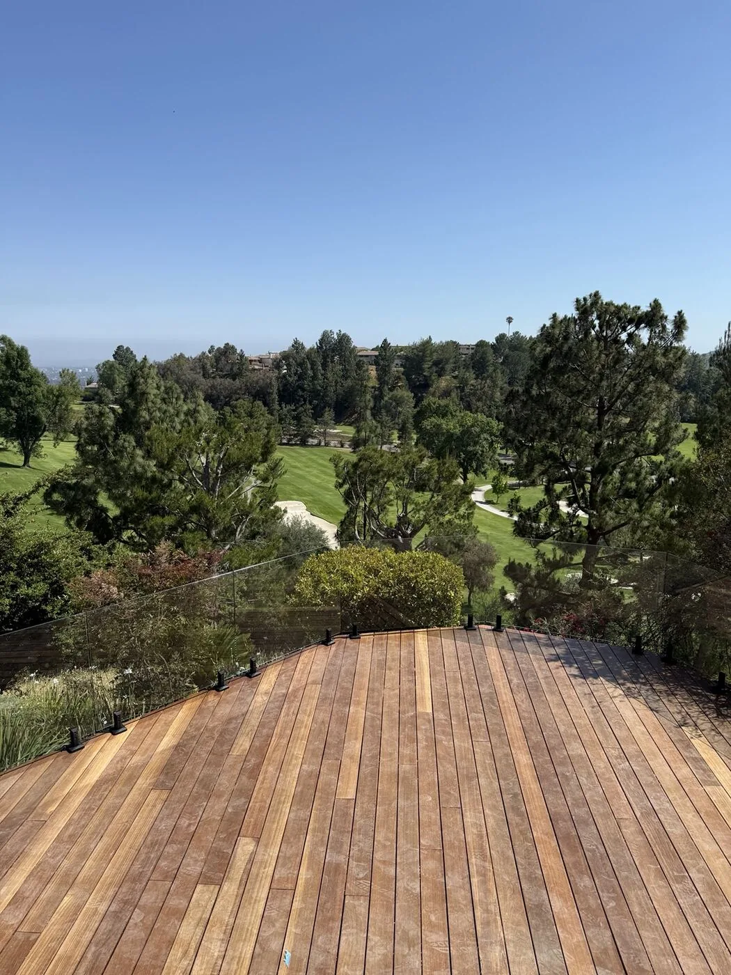 Wood deck with frameless glass railing overlooking the golf course and hills
